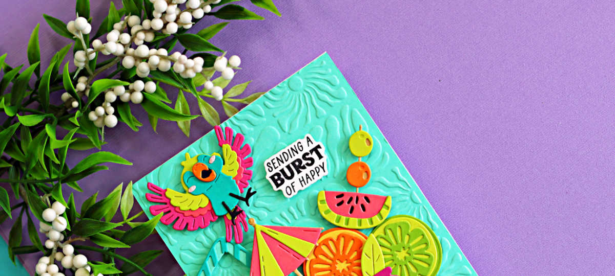 Colorful tropical die cut card featuring a bright parrot, citrus slices, watermelon, and umbrella created with the Spellbinders May Large Die of the Month. The aqua embossed background from the Radiant Day 3D Embossing Folder adds sunny texture to this Caribbean color splash summer card design.