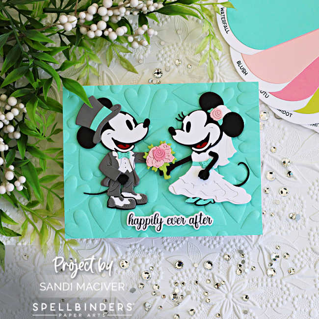 Handmade wedding card featuring die cut classic mouse bride and groom characters from Spellbinders on a mint embossed heart background with a “happily ever after” sentiment. The card is accented with blush pink flowers, layered die cuts, sparkling gems, and soft mint, pink, gray, black, and white cardstock.