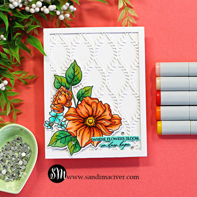 Handmade floral card featuring a framed white lattice background created with the Simon Says Stamp Willowweave Plate and colorful Copic-colored flowers from the Blooms of Encouragement stamp set. The dimensional card design includes bright orange florals, layered die cuts, a clean white frame, and a soft coral crafting backdrop with Copic markers and embellishments.