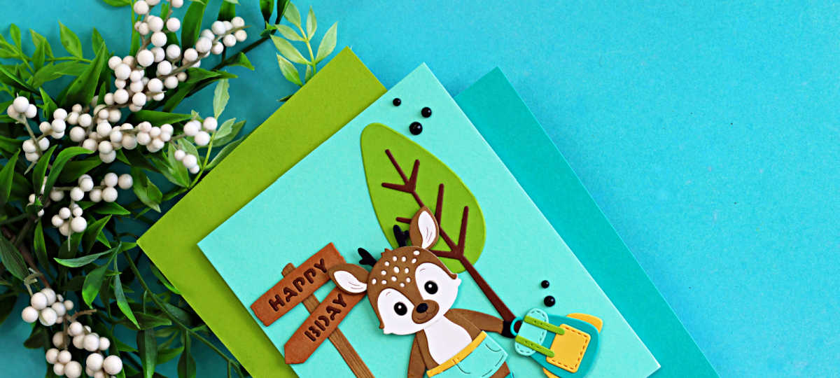 Cute summer camp die cut birthday card featuring a layered woodland deer holding a backpack beside a Happy Birthday sign, created with the Spellbinders Summer Camp Collection by Alli Fraser in teal, green, brown, and yellow cardstock.