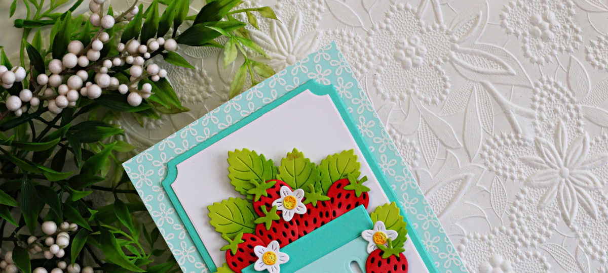 Close up of a handmade strawberry basket card featuring layered die cut strawberries, green leaves, and tiny white flowers inside a soft aqua basket. The card includes white heat embossed floral details on Seaside cardstock with layered A2 Notched Rectangle frames in white and Waterfall cardstock.