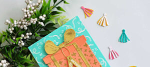Handmade easy birthday card idea featuring the Hero Arts My Monthly Hero Big Present Die Set with peach and gold die cut gift box, gold heat embossing, aqua background, and colorful die cut tassel embellishments.