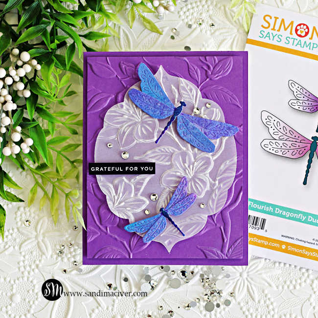 Elegant handmade dragonfly card featuring embossed vellum floral layers over a rich purple embossed background with shimmering blue and violet dragonflies colored using Lindy’s Magicals in Sweet Violet Purple and Hydrangea Blue.