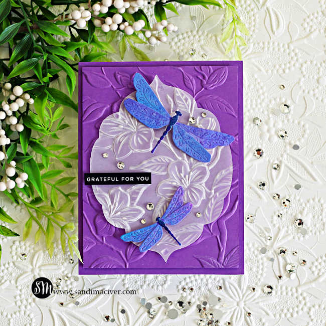 Elegant handmade dragonfly card featuring embossed vellum floral layers over a rich purple embossed background with shimmering blue and violet dragonflies created using Lindy’s Magicals in Sweet Violet Purple and Hydrangea Blue.