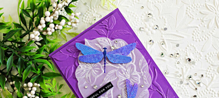 Elegant handmade card featuring shimmering blue and purple dragonflies layered over an embossed vellum floral panel on a rich purple embossed background, created with Simon Says Stamp Flourish Dragonfly Duo dies and Apple Blossoms embossing folder.