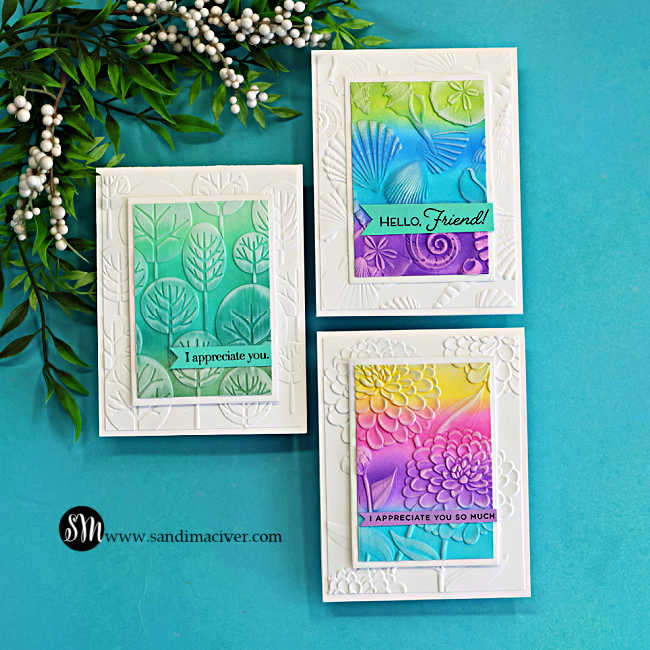Set of three handmade cards featuring embossing folder backgrounds with die cut frames, ink blended panels in rainbow and teal tones, and white ink highlighting the embossed details