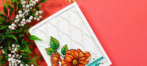Close-up of a handmade card featuring a framed white lattice background created with the Simon Says Stamp Willowweave Plate. The card showcases vibrant orange Copic-colored florals from the Blooms of Encouragement stamp set, layered over the dimensional die cut background with a clean white frame and soft coral backdrop.