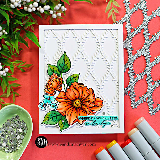 Handmade floral card featuring a framed white lattice background created with the Simon Says Stamp Willowweave Plate and colorful Copic-colored flowers from the Blooms of Encouragement stamp set. The dimensional card design includes bright orange florals, layered die cuts, a clean white frame, and a soft coral crafting backdrop with Copic markers and embellishments.