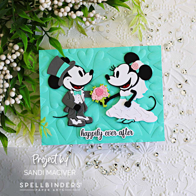 Handmade wedding card featuring die cut classic mouse bride and groom characters from Spellbinders on a Waterfall blue embossed heart background with a “happily ever after” sentiment. The card includes blush pink floral accents, layered die cuts, sparkling gems, and a soft Waterfall blue, pink, gray, black, and white color palette.