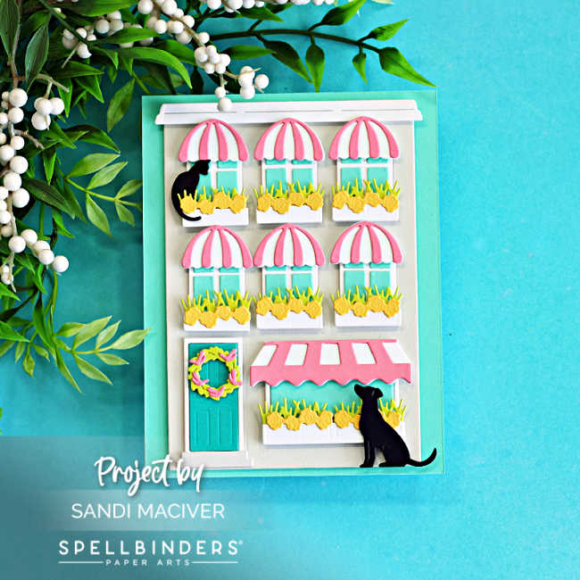Layered die cut city storefront card featuring pink striped awnings, flower-filled window boxes, black cats, and dimensional details created with the Spellbinders Yana’s Everyday City Holiday dies in soft spring colors of Fog, Teal Topaz, Waterfall, Peridot, Tutu, and black cardstock.