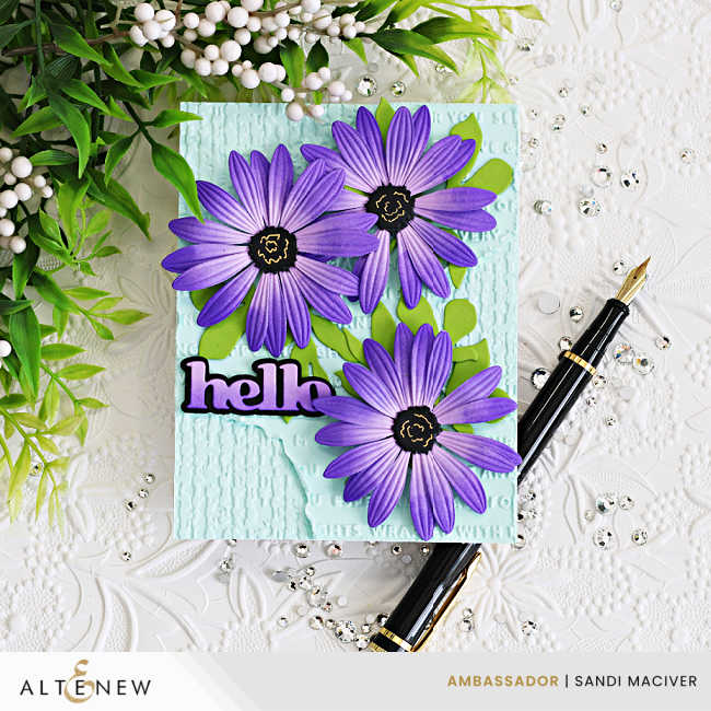 Handmade Altenew card featuring three layered purple African daisies with embossed petals and black centers arranged over a soft aqua mixed-media background with embossed texture, distressed details, bright green leaves, and a bold “hello” sentiment.