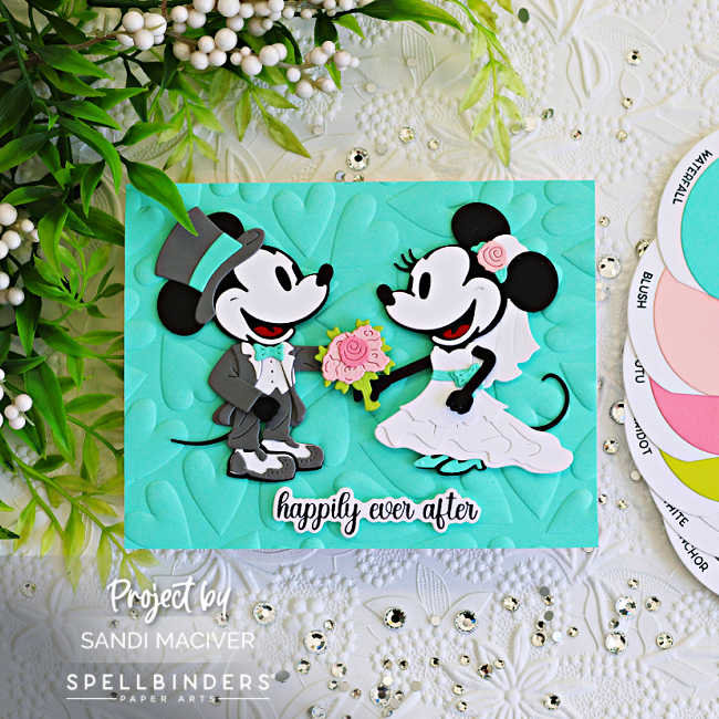 Handmade wedding card featuring die cut classic mouse bride and groom characters from Spellbinders on a Waterfall blue embossed heart background with a “happily ever after” sentiment. The card includes blush pink floral accents, layered die cuts, sparkling gems, and a soft Waterfall blue, pink, gray, black, and white color palette.