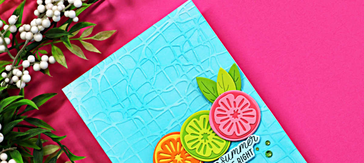 Close-up of a bright summer handmade card featuring layered citrus die cuts in pink, lime, and orange on a turquoise embossed background created with the Spellbinders May Embossing Folder Club.