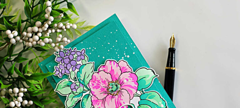 Spring floral card featuring layered stenciled pink and purple flowers with mint green leaves on a deep teal background with white splatter and fountain pen styling accents.