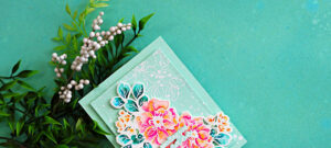 Handmade floral sympathy card featuring vibrant watercoloring with Karin Markers, pink and coral Wild Rose flowers, teal leaves, white splatter details, and layered mint green cardstock against a soft aqua background.