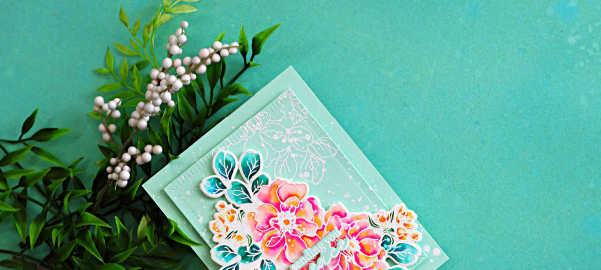 Handmade floral sympathy card featuring vibrant watercoloring with Karin Markers, pink and coral Wild Rose flowers, teal leaves, white splatter details, and layered mint green cardstock against a soft aqua background.