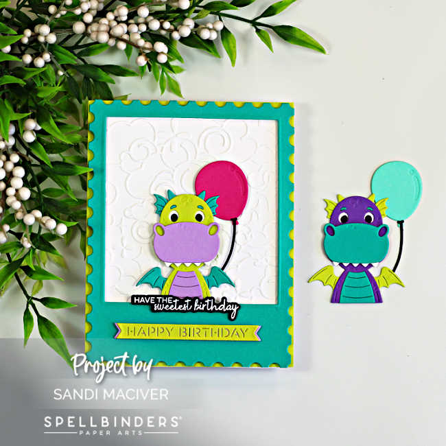Handmade birthday card featuring the Spellbinders Party Time Dragon peeking through a teal polaroid-style frame. The lime green and lavender dragon holds a bright pink balloon against a white embossed Cloud Nine background. A coordinating purple and teal dragon with a mint balloon is displayed beside the card, while leafy greenery with white berries accents the scene. The cheerful design includes layered die cuts, dimension, and birthday sentiments.