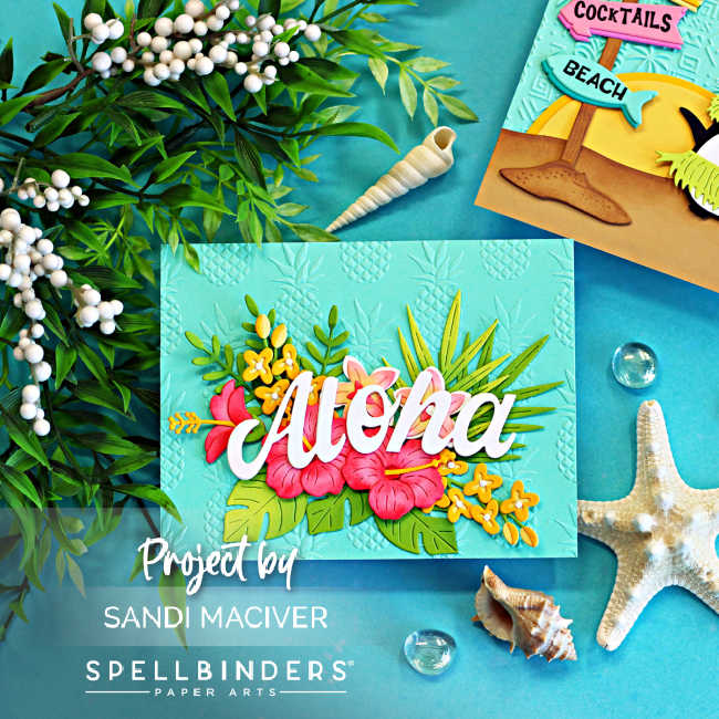 Handmade tropical Aloha card featuring bright pink hibiscus flowers, layered tropical foliage, and a large white "Aloha" sentiment on an aqua background embossed with a pineapple pattern. The card is photographed with starfish, seashells, greenery, and glass gems on a turquoise backdrop, creating a relaxing island-inspired beach scene.