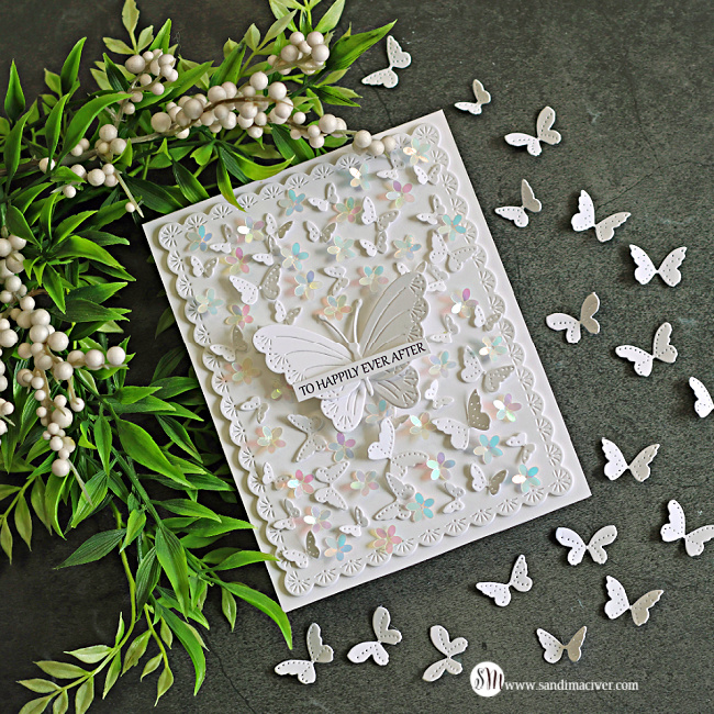 Elegant all-white butterfly card featuring layered die-cut butterflies, iridescent floral embellishments, and a delicate scalloped frame. A dimensional butterfly centerpiece displays a "To Happily Ever After" sentiment, surrounded by fluttering butterflies and photographed on a dark stone background with greenery and berry stems.