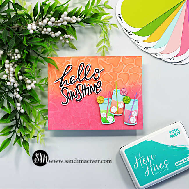Summer-themed handmade card featuring a bright pink and orange ink-blended background with a layered water ripple stencil design. The card includes colorful tropical drink die cuts with citrus garnishes, ice cubes, and straws, paired with a bold black and white “hello sunshine” sentiment. Hero Arts ink pad and cardstock swatches are displayed beside the card.