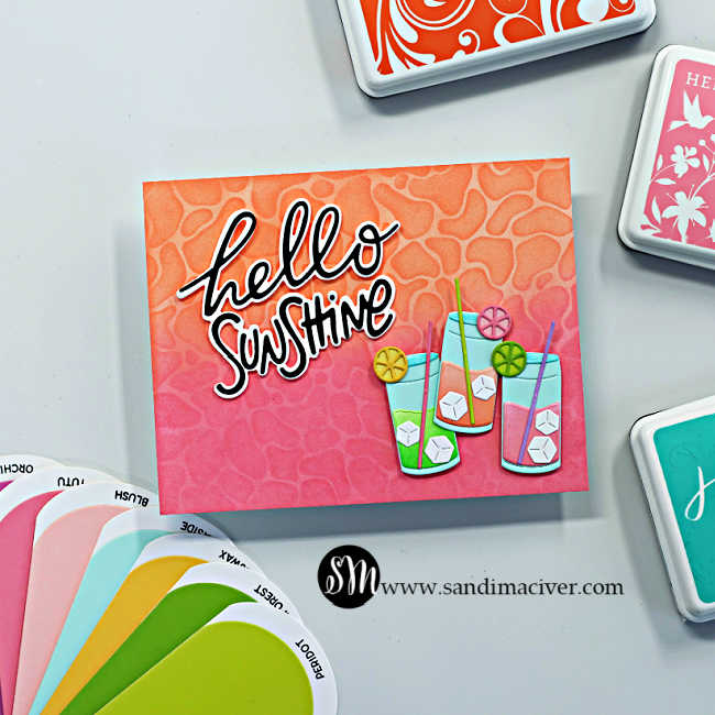 Bright summer-themed handmade card featuring a pink and orange ink-blended background with a layered water ripple stencil design. The card is decorated with colorful tropical drink die cuts, citrus slice accents, ice cubes, and a bold black and white “hello sunshine” sentiment. Coordinating cardstock swatches and Hero Arts ink pads frame the card for a bright tropical summer feel.