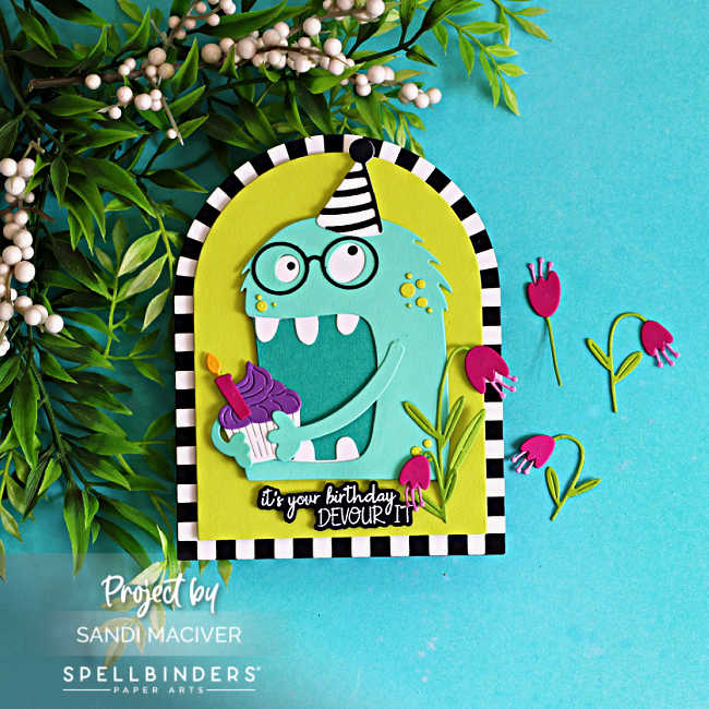 Handmade shaped birthday card featuring Chompster, a whimsical turquoise monster wearing a black-and-white striped party hat and glasses while holding a cupcake with purple frosting and a lit candle. The monster is framed inside a lime green arch with a bold black-and-white striped border. Bright pink flowers and green foliage decorate the right side of the card, and the sentiment reads, "It's your birthday, DEVOUR IT!" The card is photographed on a turquoise background with greenery and white berries.