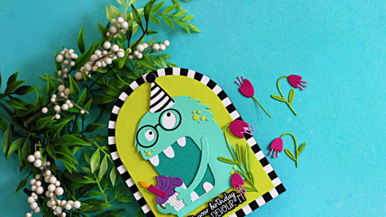 Bright and whimsical shaped birthday card featuring a turquoise Chompster monster wearing a striped party hat and holding a cupcake with a lit candle. The monster is framed inside a lime green arch with a black-and-white striped border and surrounded by pink flowers. The card sits on a blue background with decorative greenery and white berries. The sentiment reads, "It's your birthday, DEVOUR IT!"
