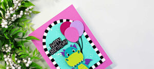 Bright and playful dragon birthday card featuring the Spellbinders Party Time Dragon die set with colorful balloons, a turquoise ink-blended background, bold black and white striped arch frame, and a happy birthday sentiment on a vibrant pink card base.