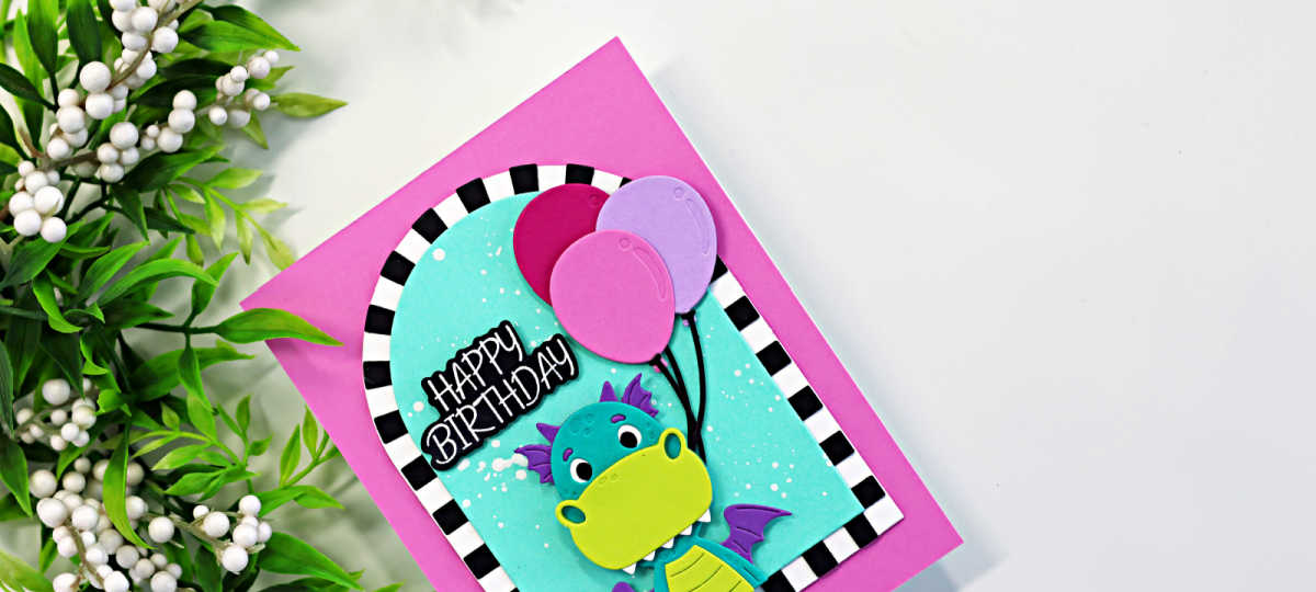 Bright and playful dragon birthday card featuring the Spellbinders Party Time Dragon die set with colorful balloons, a turquoise ink-blended background, bold black and white striped arch frame, and a happy birthday sentiment on a vibrant pink card base.