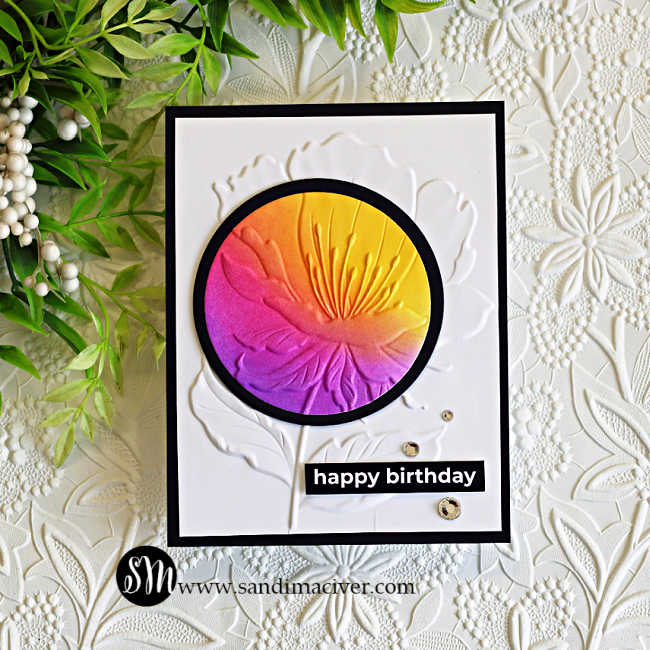 Handmade birthday card featuring the Spotlight Technique with Embossing Folders using the Simon Says Stamp Curvy Blossom 3D Embossing Folder. A vibrant ink-blended spotlight in yellow, orange, pink, and purple highlights the embossed flower against a white embossed background with a black frame and happy birthday sentiment.