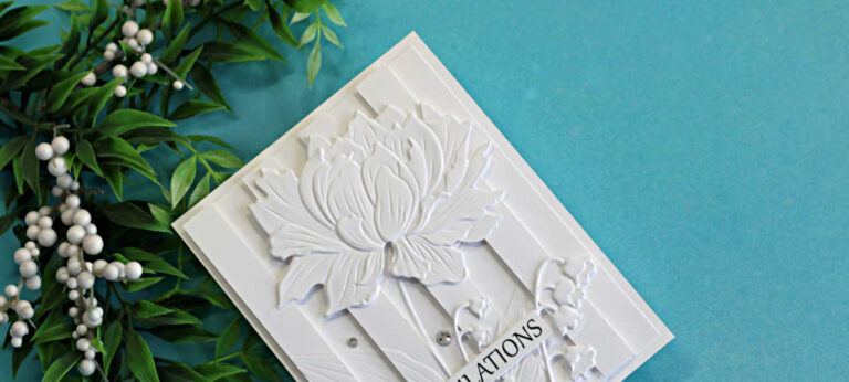 White-on-white embossed floral card featuring the Embossed Double Vision technique. A large dimensional flower and delicate floral details are layered over raised vertical panels, creating elegant depth and texture against a soft turquoise background.