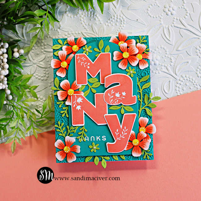 andmade floral thank you card featuring oversized coral "Many" die-cut letters layered over a teal arched panel with a textured embossed background. Coral flowers, leafy green die cuts, and a white heat-embossed "thanks" sentiment create a bright, dimensional design.