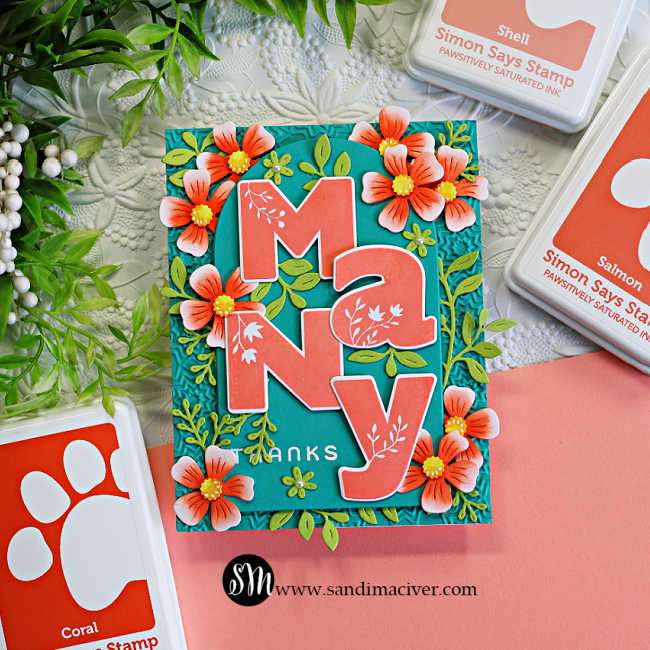 Handmade thank you card featuring oversized coral "Many" die-cut letters layered over a teal arched panel with a subtle embossed background. Coral flowers and leafy green die cuts frame the sentiment, while Simon Says Stamp Coral, Salmon, and Shell ink pads surround the card.