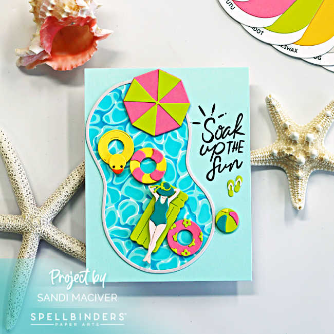 Handmade summer pool card featuring a die-cut swimming pool filled with bright aqua water, colorful floaties, a yellow rubber duck tube, beach umbrella, flip-flops, and a relaxing swimmer. The card includes the sentiment “Soak Up the Fun” on a soft aqua background with beach-inspired seashell and starfish accents.