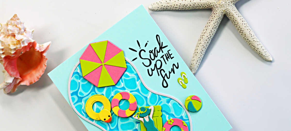 Bright and cheerful summer pool card featuring a blue swimming pool die cut filled with colorful floaties, including a yellow rubber duck tube, pink and lime life preservers, a beach umbrella, flip-flops, and a relaxing swimmer. The card includes the sentiment “Soak Up the Fun” on a soft aqua background with beach-inspired seashell and starfish props.