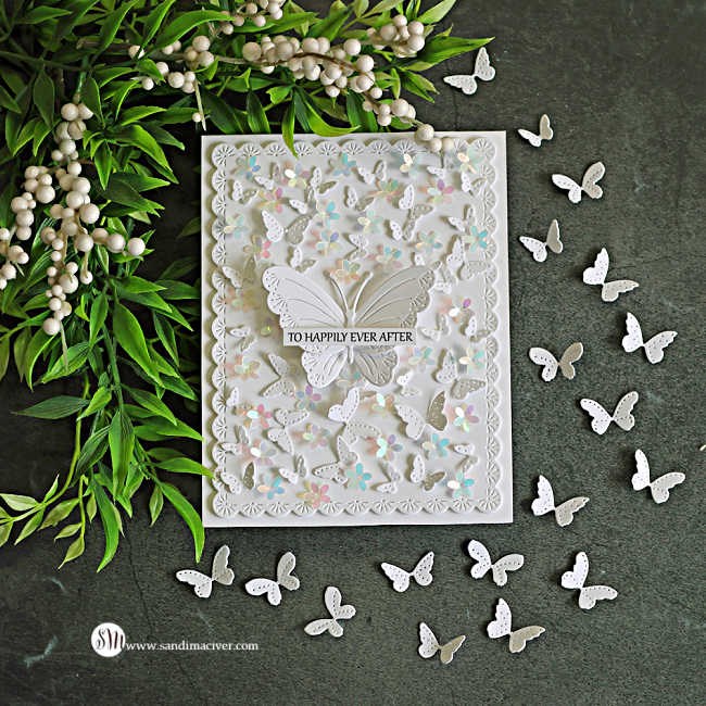 Elegant all-white butterfly card featuring layered die-cut butterflies, iridescent floral embellishments, and a delicate scalloped frame. A dimensional butterfly centerpiece displays a "To Happily Ever After" sentiment, surrounded by fluttering butterflies and photographed on a dark stone background with greenery and berry stems.