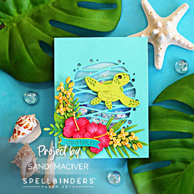 Handmade tropical shaker card featuring a layered green sea turtle swimming over a blue ocean-inspired shaker window filled with sequins. Bright pink hibiscus flowers, yellow tropical blooms, and lush green foliage decorate the bottom of the card. The card is photographed on a turquoise background with tropical monstera leaves and starfish accents, creating a Hawaiian paradise theme.