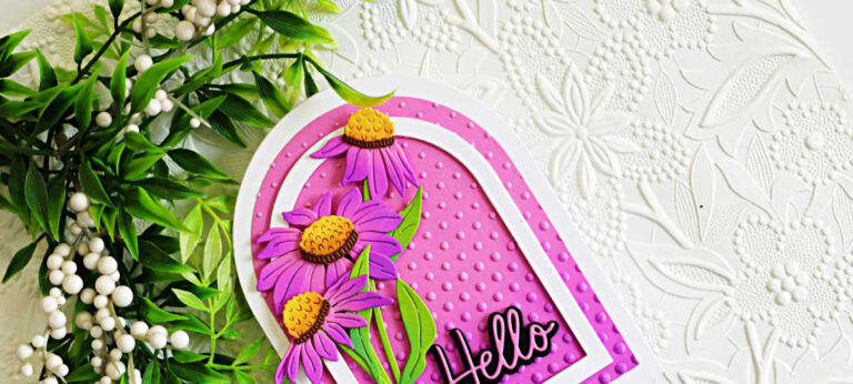 Close-up of a handmade arched floral greeting card featuring layered purple wild cornflowers with yellow centers and bright green leaves. The flowers are arranged inside a white arched frame over a pink embossed background created with the Cascading Dots Embossing Folder. A black "Hello" sentiment sits at the bottom of the arch, while a white embossed floral background and greenery complete the elegant garden-inspired