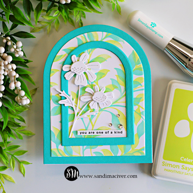 Handmade arched greeting card featuring a soft pastel Leafy Greens stenciled background, layered Audrey Blue arch frames, and white layered Quirky Daisies. The floral arrangement is accented with Clear Dazzling Gems and a "you are one of a kind" sentiment, and photographed with a Simon Says Stamp blending brush and Celery ink pad.
