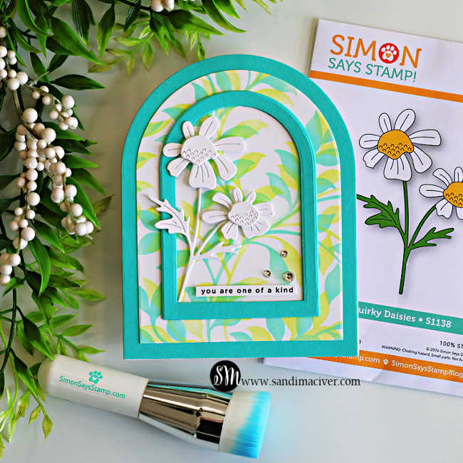 Handmade arched greeting card featuring a soft pastel Leafy Greens stenciled background, layered Audrey Blue arch frames, and white layered die-cut Quirky Daisies. The floral design is finished with a "you are one of a kind" sentiment and Clear Dazzling Gems, and displayed beside the Simon Says Stamp Quirky Daisies die set and a blending brush.