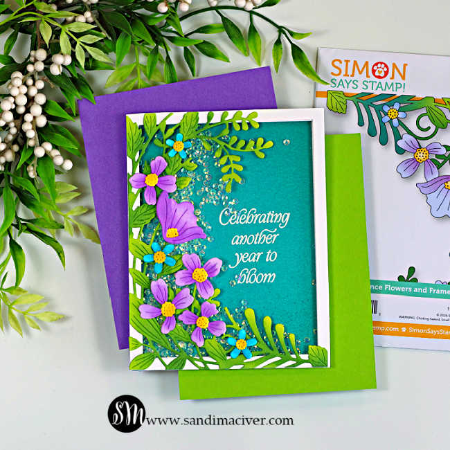 Handmade easy floral shaker birthday card featuring the Simon Says Stamp Leaf Dance Flowers and Frame die. Ink-blended green foliage and purple flowers frame a teal shaker window filled with sparkling clear sequins. The white embossed sentiment reads, "Celebrating another year to bloom." The card is photographed with the Leaf Dance Flowers and Frame die packaging and colorful cardstock on a white background.