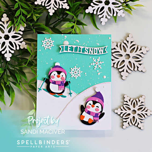 Handmade Christmas card featuring two adorable die-cut penguins from the Spellbinders Snow Much Fun Small Die of the Month. One penguin skis down a snowy hill while the other sleds below, surrounded by white snowflakes and a "Let It Snow" sentiment against a teal ink-blended winter sky.