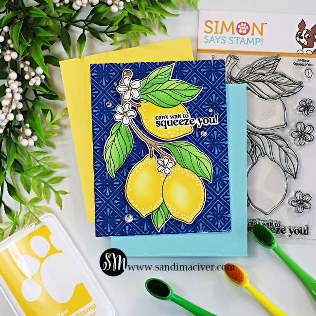 A handmade lemon-themed greeting card featuring two bright yellow lemons, green leaves, and white blossoms on a deep navy blue embossed background highlighted with white pigment ink to resemble Spanish ceramic tiles. The sentiment, "can't wait to squeeze you!", is layered over the top lemon. The card is displayed on yellow and light blue cardstock alongside the coordinating Simon Says Stamp Squeeze You stamp set, yellow and green ink pads, blending brushes, and greenery on a white work surface.