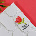 Handmade white birthday card featuring a geometric pattern created with oval die cuts over an embossed background, accented with a coral flower and Happy Birthday sentiment.