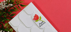 Handmade white birthday card featuring a geometric pattern created with oval die cuts over an embossed background, accented with a coral flower and Happy Birthday sentiment.