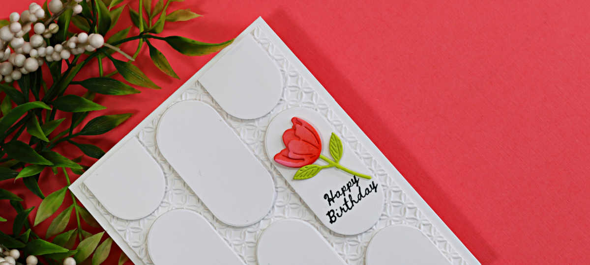 Handmade white birthday card featuring a geometric pattern created with oval die cuts over an embossed background, accented with a coral flower and Happy Birthday sentiment.