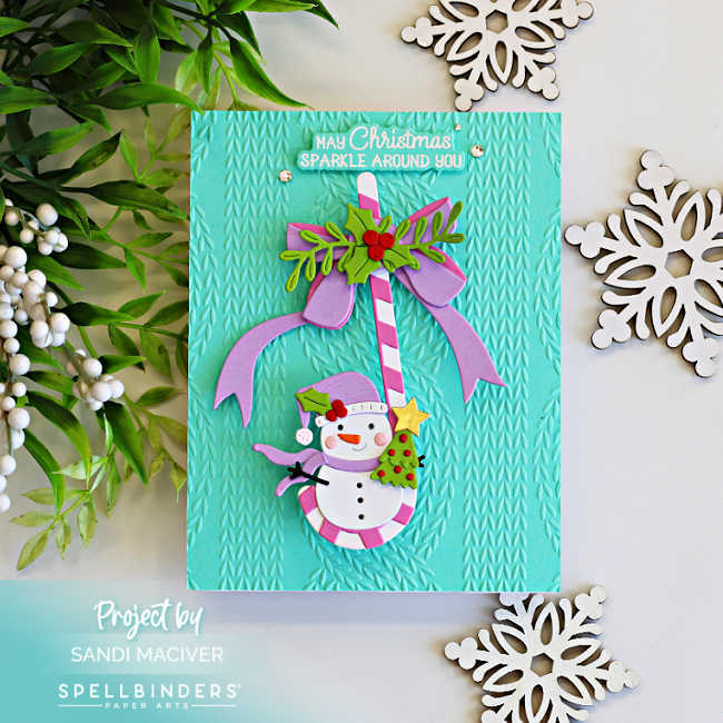 Interactive Christmas card featuring a smiling snowman suspended from a pink and white candy cane on a turquoise knit embossed background, finished with a lavender bow, holly leaves, and festive Christmas accents.