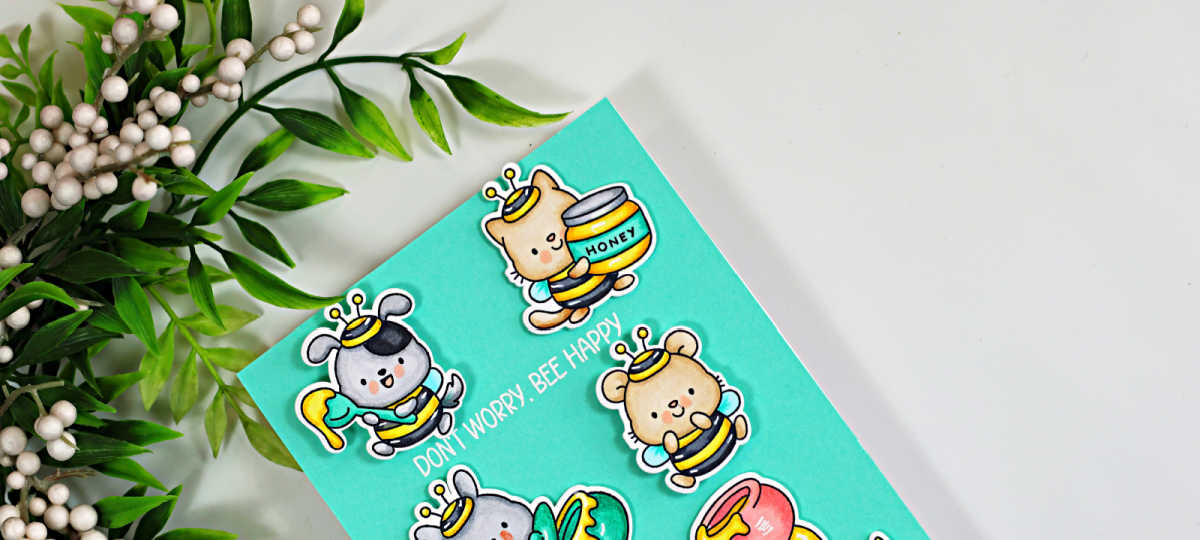 Close-up of a seafoam teal interactive card featuring Copic-colored critters dressed as bees, with a white embossed “Don’t Worry, Bee Happy” sentiment and leafy greenery in the background.