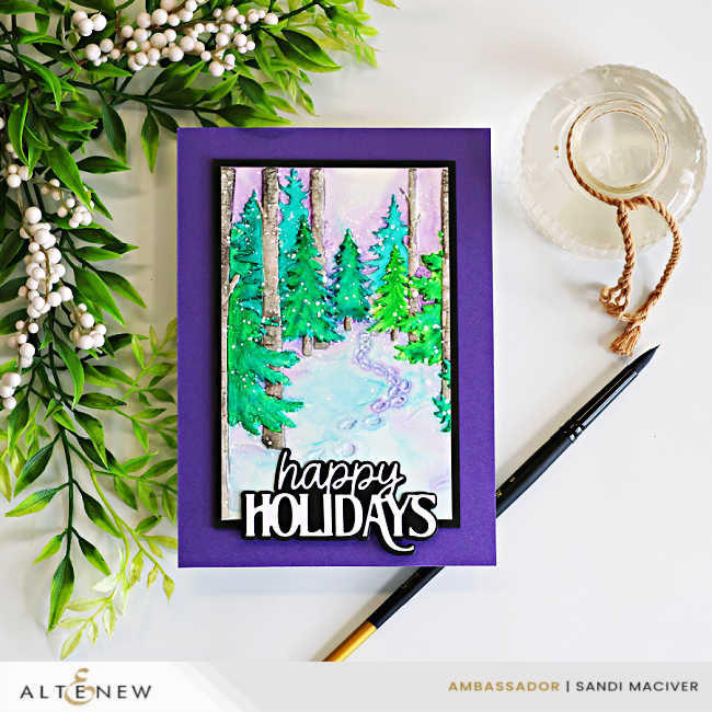 Handmade holiday card featuring a snowy forest scene created with the Altenew Snowy Footpath Embossing Folder and a loose watercolor technique. Evergreen trees, birch trunks, and a winding snow-covered path are painted in soft shades of green, turquoise, and lavender, then layered onto a rich purple card base. A bold black-and-white "happy Holidays" die-cut sentiment finishes the design, with a watercolor brush and water jar styled beside the card
