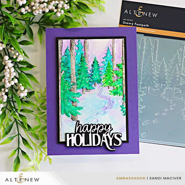 Handmade holiday card featuring a snowy forest scene created with the Altenew Snowy Footpath 3D Embossing Folder and a simple watercolor technique. Soft watercolor shades of green, turquoise, lavender, and gray highlight the embossed evergreen trees, birch trunks, and winding snow-covered path. The panel is mounted on a rich purple card base and finished with a layered black-and-white "happy Holidays" die-cut sentiment. The Altenew Snowy Footpath embossing folder package is displayed beside the finished card.